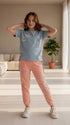 Child wearing a gray t-shirt and pink pants with 'Rama' branding in a room with plants.