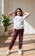 Child wearing a white t-shirt and maroon pants with smiley face designs, standing in a room with plants.