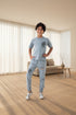 Child wearing a gray outfit with 'Rama Kids Wear' branding, standing against a white curtain background.