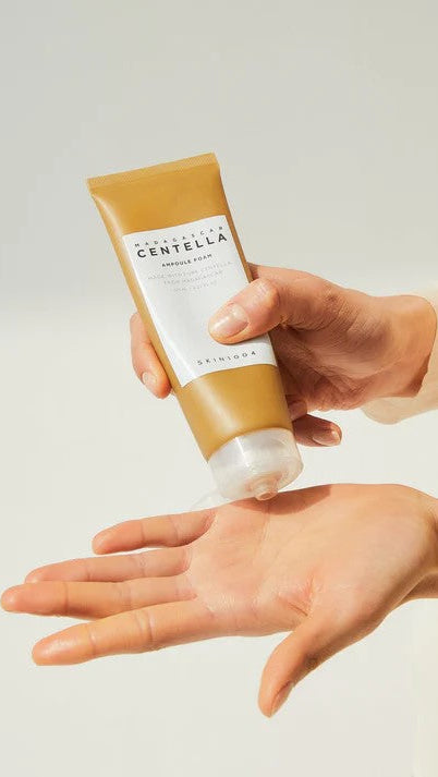 Person holding a tube of Centella Asiatica cream against a neutral background